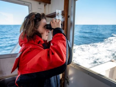 La biologiste marine Christy Hudak cherche des baleines à l'aide de jumelles, lors d'une expédition scientifique dans la baie du cap Cod, au large du Massachussets, le 5 avril 2022 - Joseph Prezioso [AFP]
