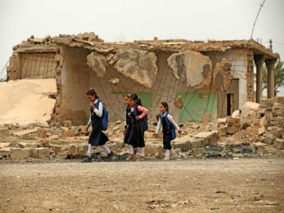 Des écolières passent devant une maison détruite à Habach, dans le nord de l'Irak, le 25 avril 2022 - AHMAD AL-RUBAYE [AFP]