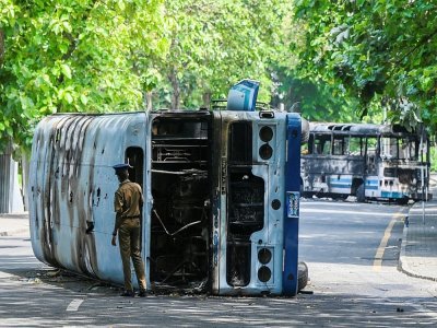 Un policier inspecte un bus brûlé à la suite des manifestations antigouvernementales à Colombo, capitale du Sri Lanka, le 10 mai 2022 - ISHARA S. KODIKARA [AFP]