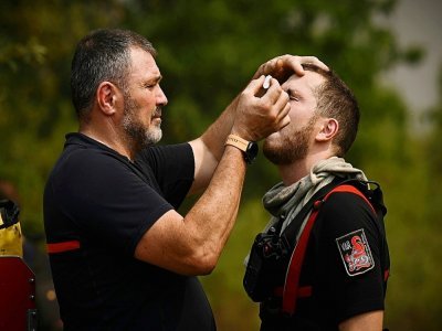 Un pompier insère des gouttes ophtalmiques dans les yeux d'un de ses collègues près de Saint-Magne (sud-ouest) le 11 août 2022 - Philippe LOPEZ [AFP]