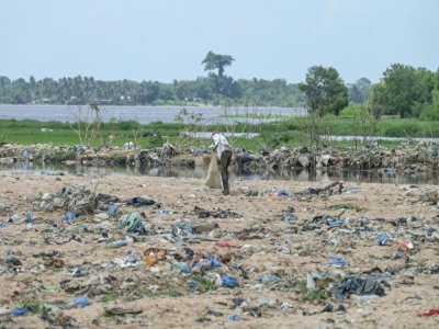 Un homme ramasse du plastique et d'autres déchets sur les rives de la lagune Ébrié près du village de Béago, à Abidjan, le 20 juillet 2022 - Sia KAMBOU [AFP]