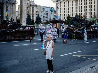 Une femme porte des ballons de baudruche devant des chars russes détruits sur une avenue centrale de Kiev, à la veille de la fête nationale de l'Ukraine, le 23 août 2022 - Dimitar DILKOFF [AFP]