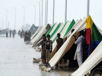 Des déplacés ayant fui leurs maisons inondées devant des tentes temporaires installées le long d'une route lors de fortes pluies de mousson à Sukkur, dans la province de Sindh, au Pakistan, le 27 août 2022 - Asif HASSAN [AFP]