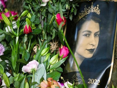 Un portrait d'Elizabeth II est vu à côté de bouquets de fleurs disposés à l'extérieur du palais de Buckingham Palace à Londres le 11 septembre 2022 - STEPHANE DE SAKUTIN [AFP]