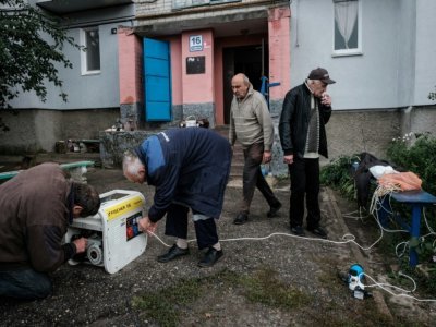 Des habitants branchent un générateur pour recharger téléphones et lampes de poche devant leur immeuble privé d'électricité  en raison des combats, le 24 septembre 2022 à  Koupiansk (est de l'Ukraine) - Yasuyoshi CHIBA [AFP]