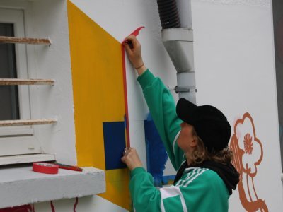 L'artiste Edith Gallot pose des bandes adhésives adaptées à la peinture. Cela permet de réaliser des formes bien droites et réaliser des perspectives qui serviront à d'autres dessins, comme un lapin qui sort d'une fenêtre.