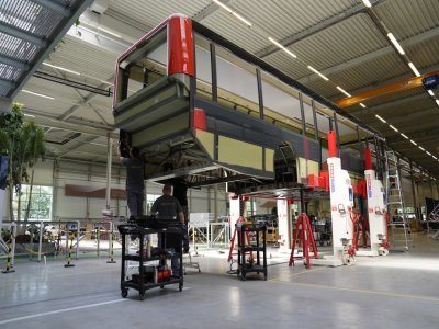 Des pièces composites en fibre de verre sont collées aux longerons en carbone, pour former les panneaux latéraux qui passent dans une machine injectant de la mousse. Il faut ensuite assembler le câblage électrique. - Ebusco