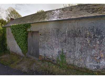 La maison est cachée derrière une haie imposante et un haut mur.