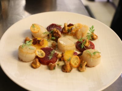 Place au dressage du plat, une étape qui demande de la précision. Il faut disposer les Saint-Jacques dans l'assiette puis les lamelles de kumquat, les girolles et ensuite parsemer d'herbes aromatiques.