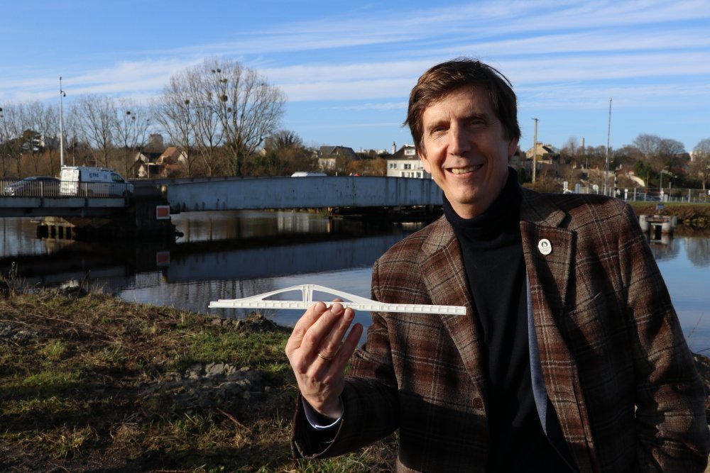 L'architecte, Thomas Lavigne, avec la maquette du nouveau pont entre les mains, devant l'actuel.